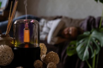 A woman resting peacefully on a sofa near plants and a lit candle, representing the self-care ritual and feel-good state created by Soapdia products.